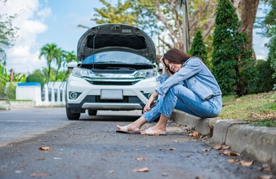 woman sitting down with broken down car on side of road